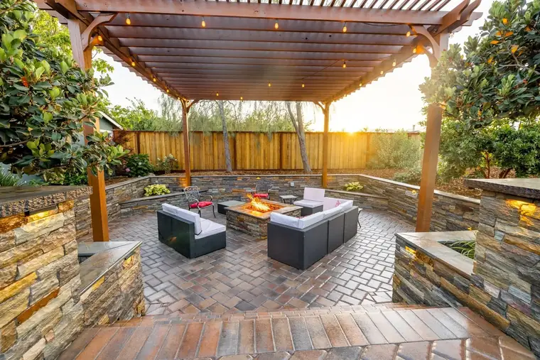 Stone seat walls and twin fire features glowing under a timber pergola at dusk