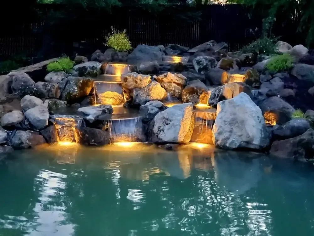 Boulder waterfall and pond glowing under night lighting