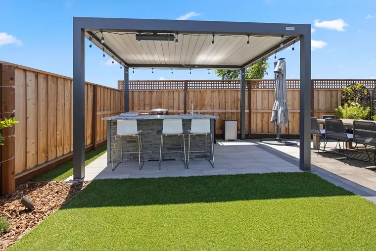 Outdoor kitchen island with stainless grill, sink, and bar seating