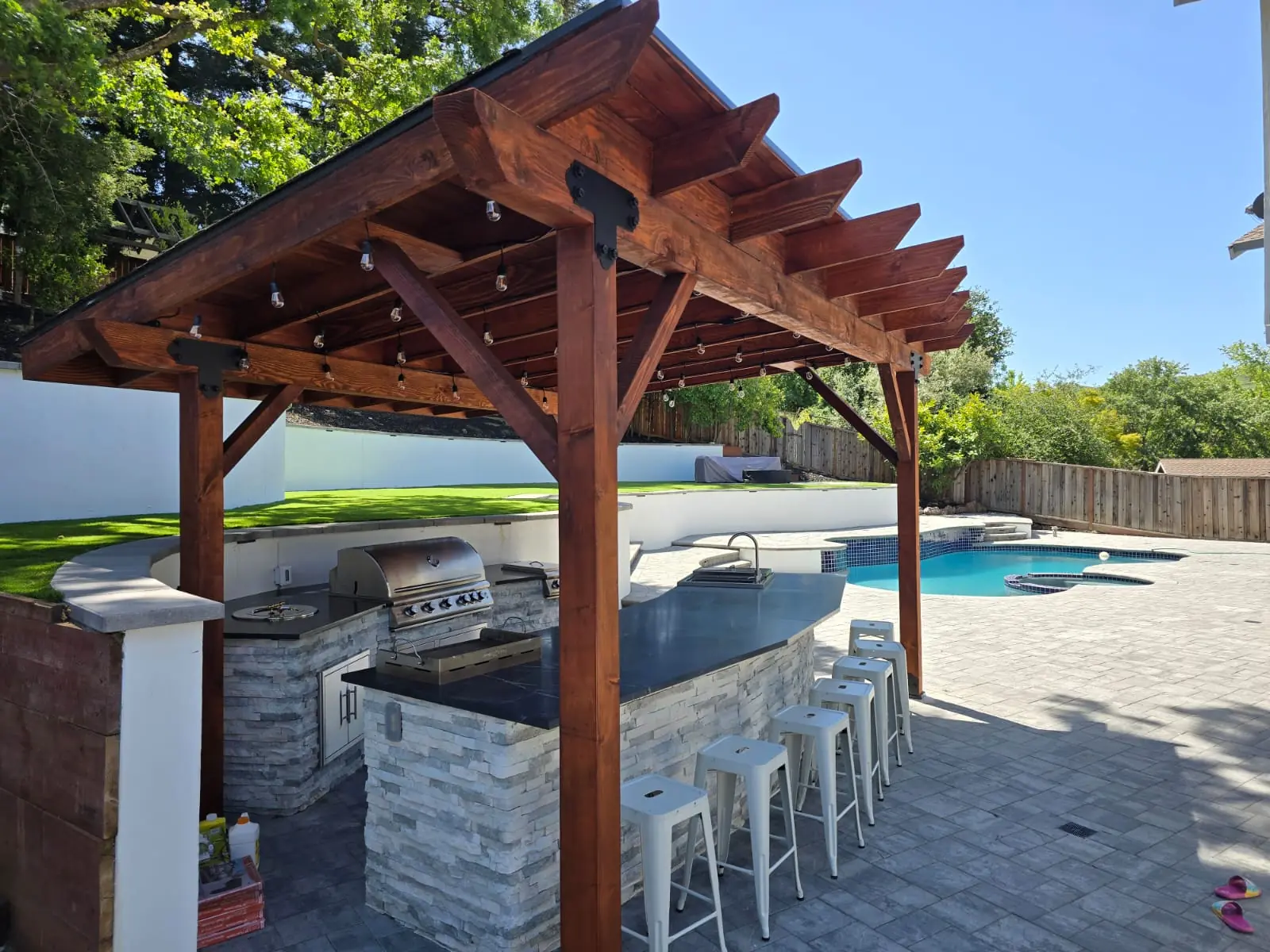 Timber pergola outdoor kitchen with bar stools beside the pool