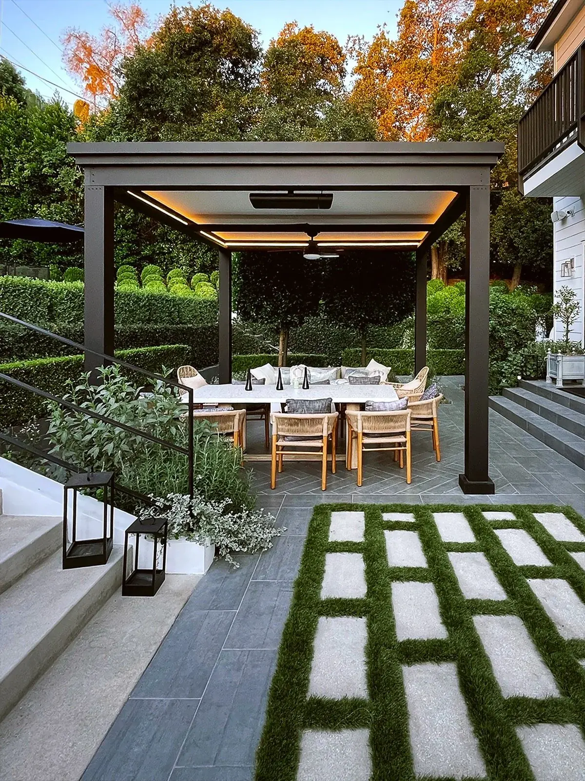 Dinner table set for eight under a lit pergola on grass-jointed pavers