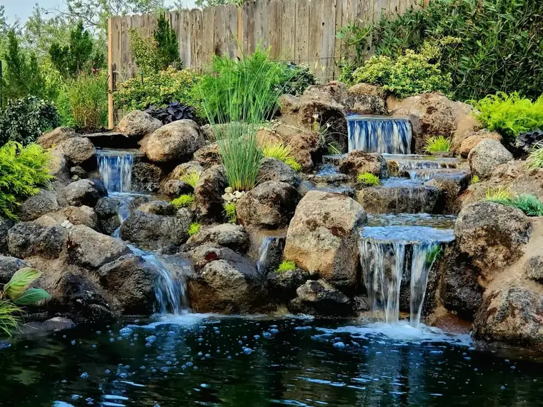 Multi-tier natural boulder waterfall spilling into a backyard pond